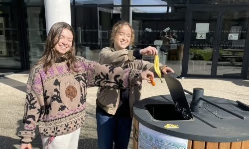 Zwei Studentinnen vor dem Komposter des Campus, eine wirft eine Bananenschale hinein